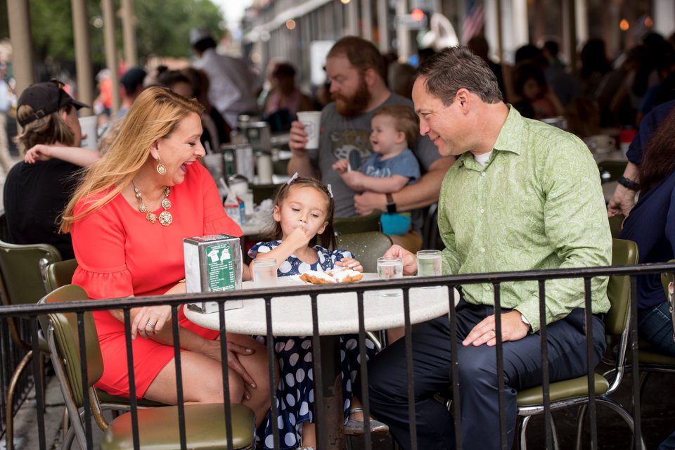 A happy family shares beignets in New Orleans at Cafe du Monde pre-COVID-19